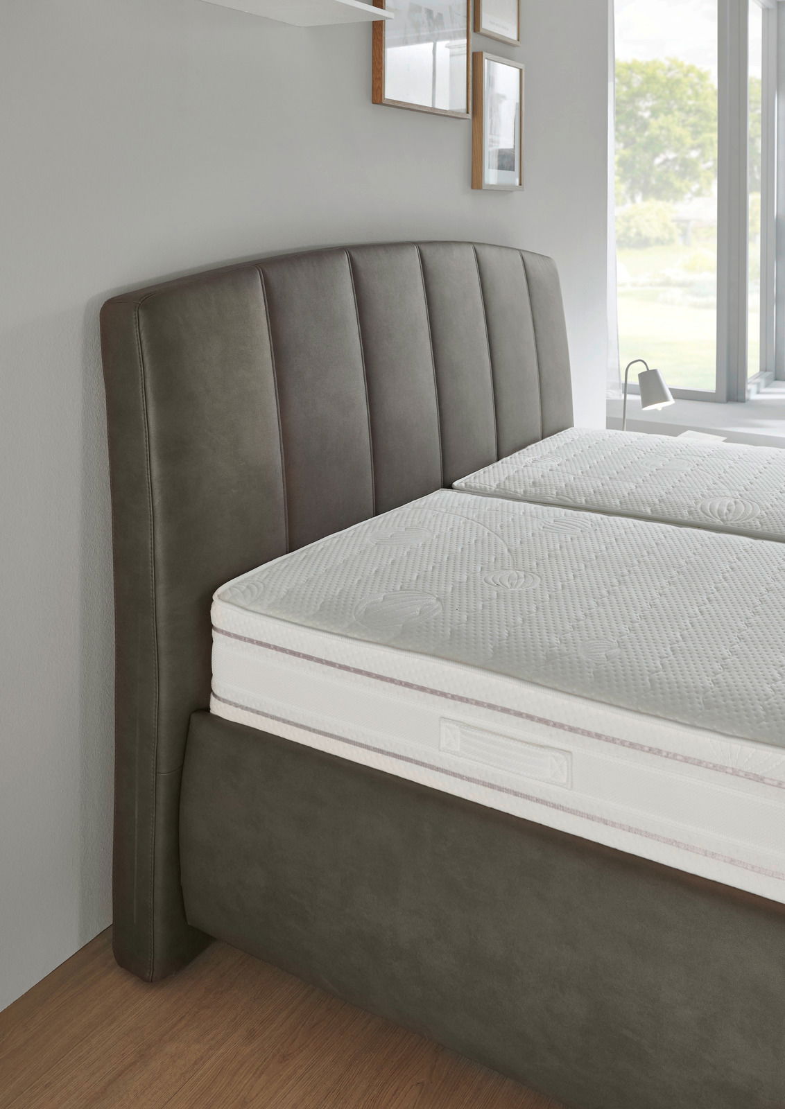 Seitliche Perspektive eines Polsterbetts mit gepolstertem Kopfteil in dunklem Stoff und einer weißen Matratze.