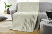 Jacquard Decke in hellem Beige mit Pflanzenmuster, drapiert über einem grauen Sofa in einem modernen Wohnzimmer, seitliche Perspektive.