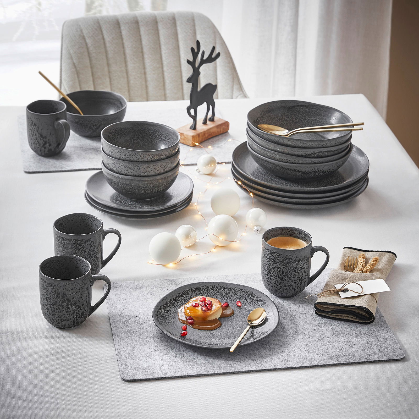 Ein stilvolles, 20-teiliges Kombiservice in dunklem Design, präsentiert auf einem festlich gedeckten Tisch mit Dekorationen. Perspektive von oben.