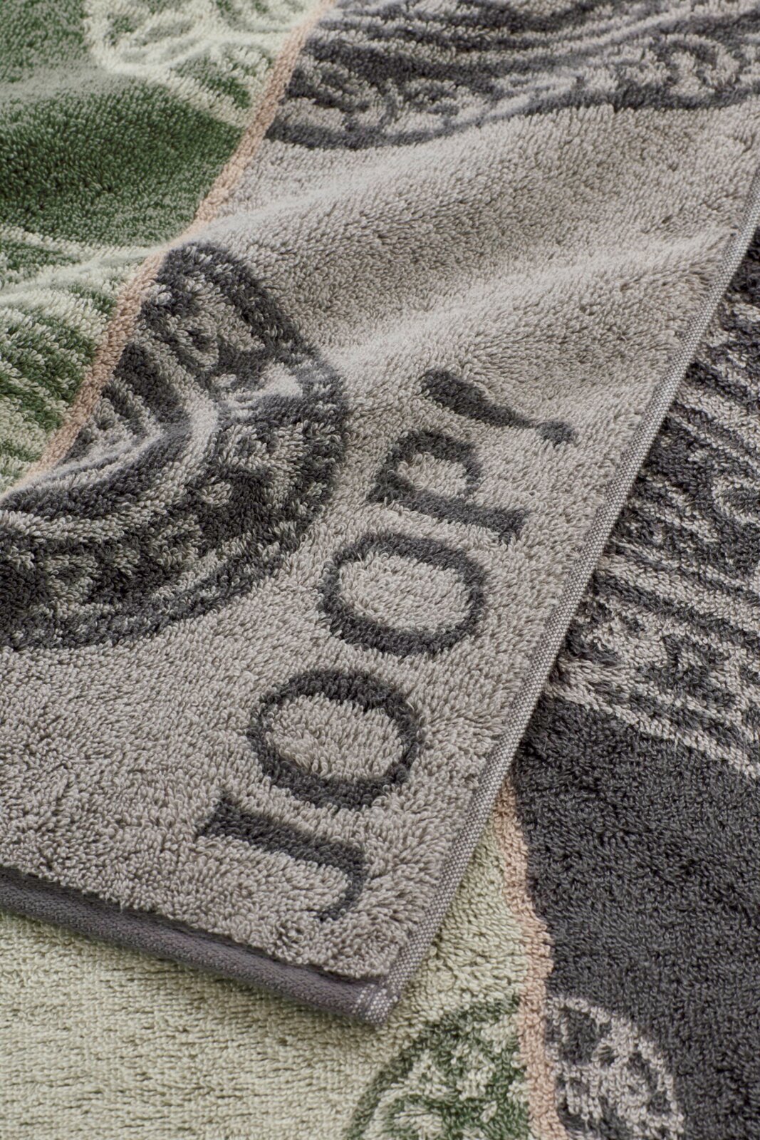 JOOP! Handtuch 50x100cm CONTOUR Detailaufnahme eines flauschigen Frottee-Handtuchs mit floraler Musterung in Grau und Grün, schräg von oben fotografiert