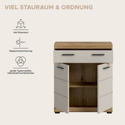 Badezimmer-Unterschrank in Holzoptik mit weißer Front und schwarzen Griffen, zwei Türen geöffnet und Innenfächer sichtbar, frontal aus leicht erhöhter Perspektive vor hellem Hintergrund mit Hinweis-Icons zu Stauraum, Kippschutz und Kombinierbarkeit.