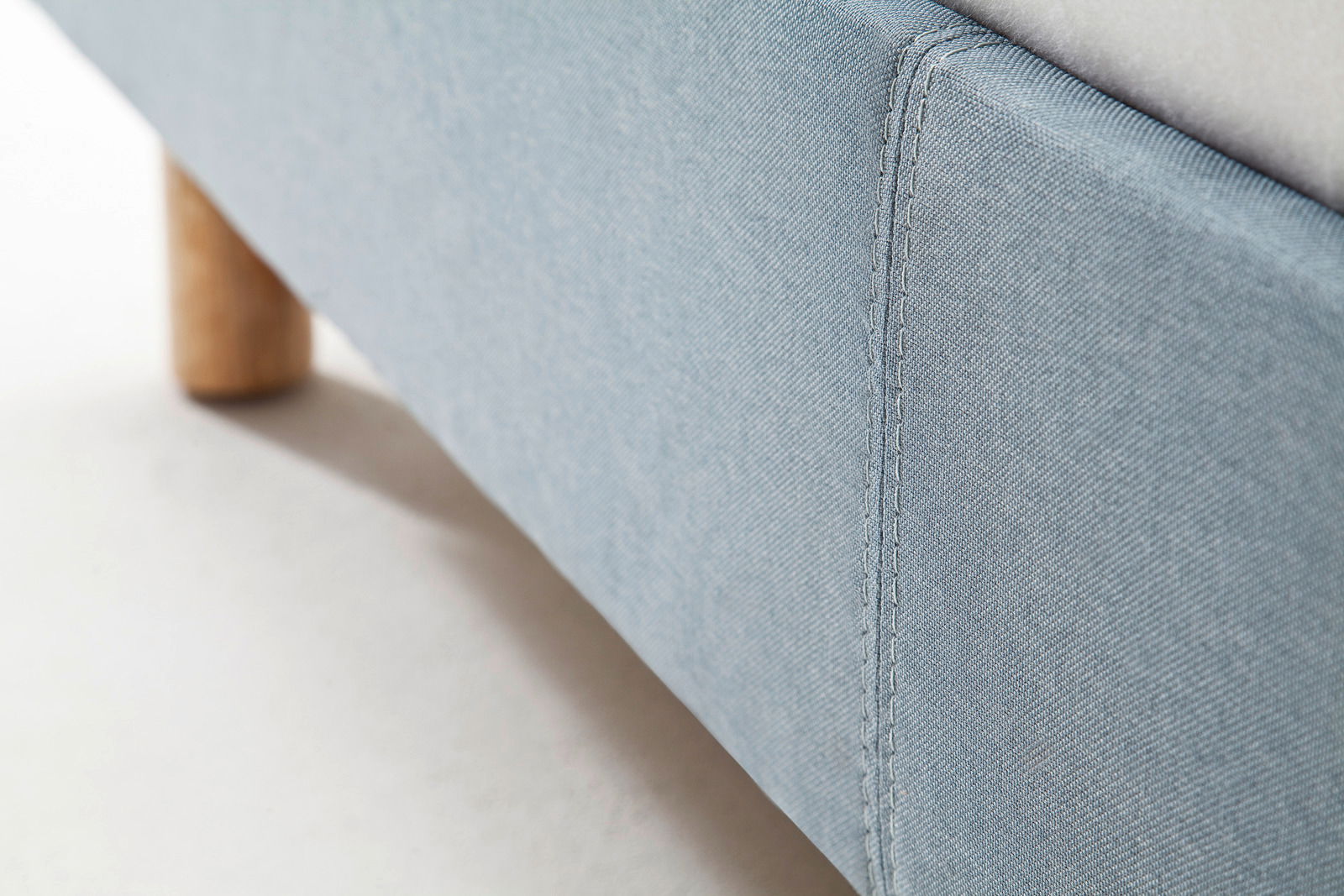 Nahaufnahme eines blauen Polsterbetts mit Holzfuß, seitliche Perspektive