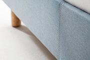Nahaufnahme eines blauen Polsterbetts mit Holzfuß, seitliche Perspektive
