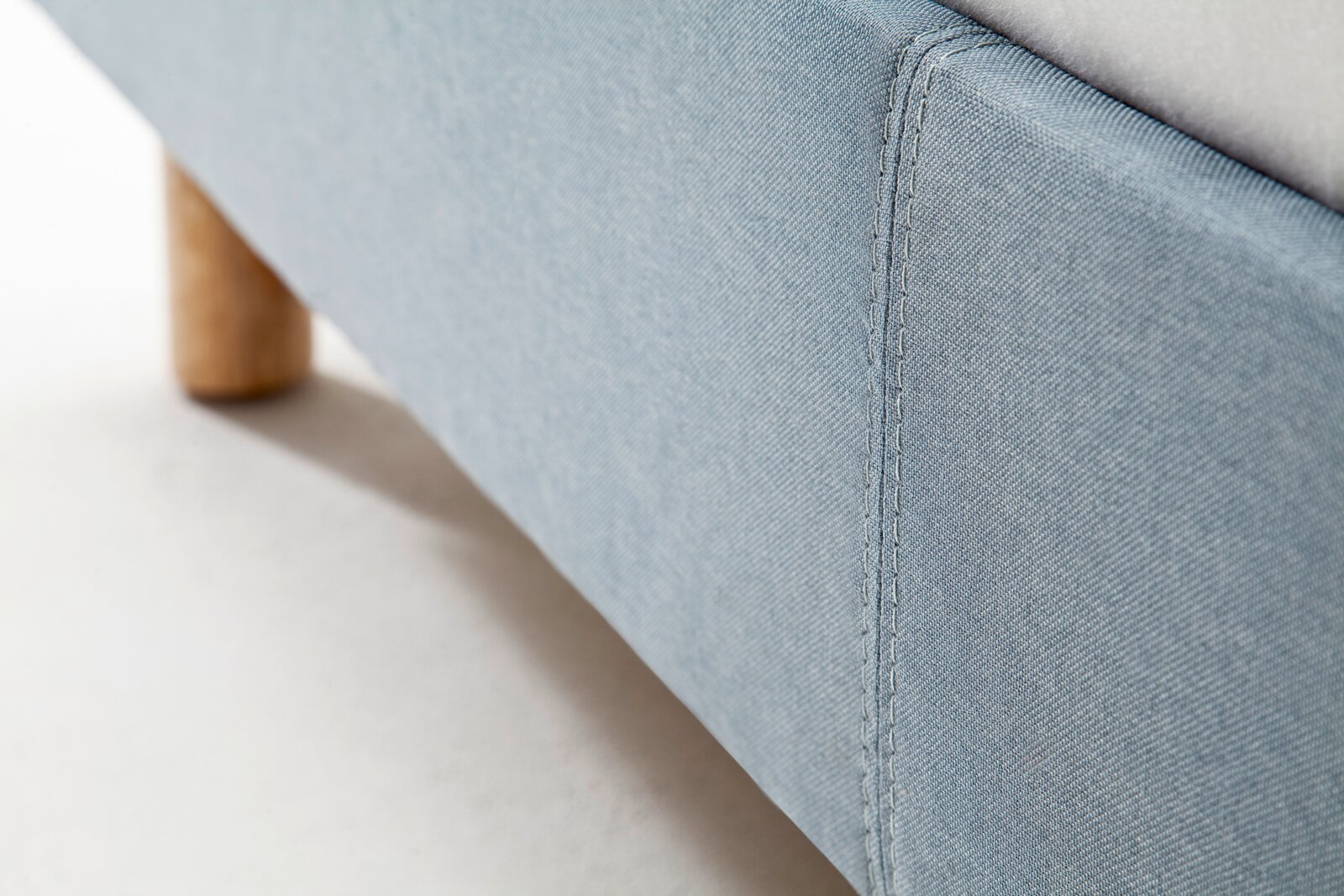 Close-up van een blauw gestoffeerd bed met houten onderstel, gezien vanaf de zijkant