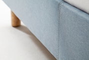 Close-up van een blauw gestoffeerd bed met houten onderstel, gezien vanaf de zijkant