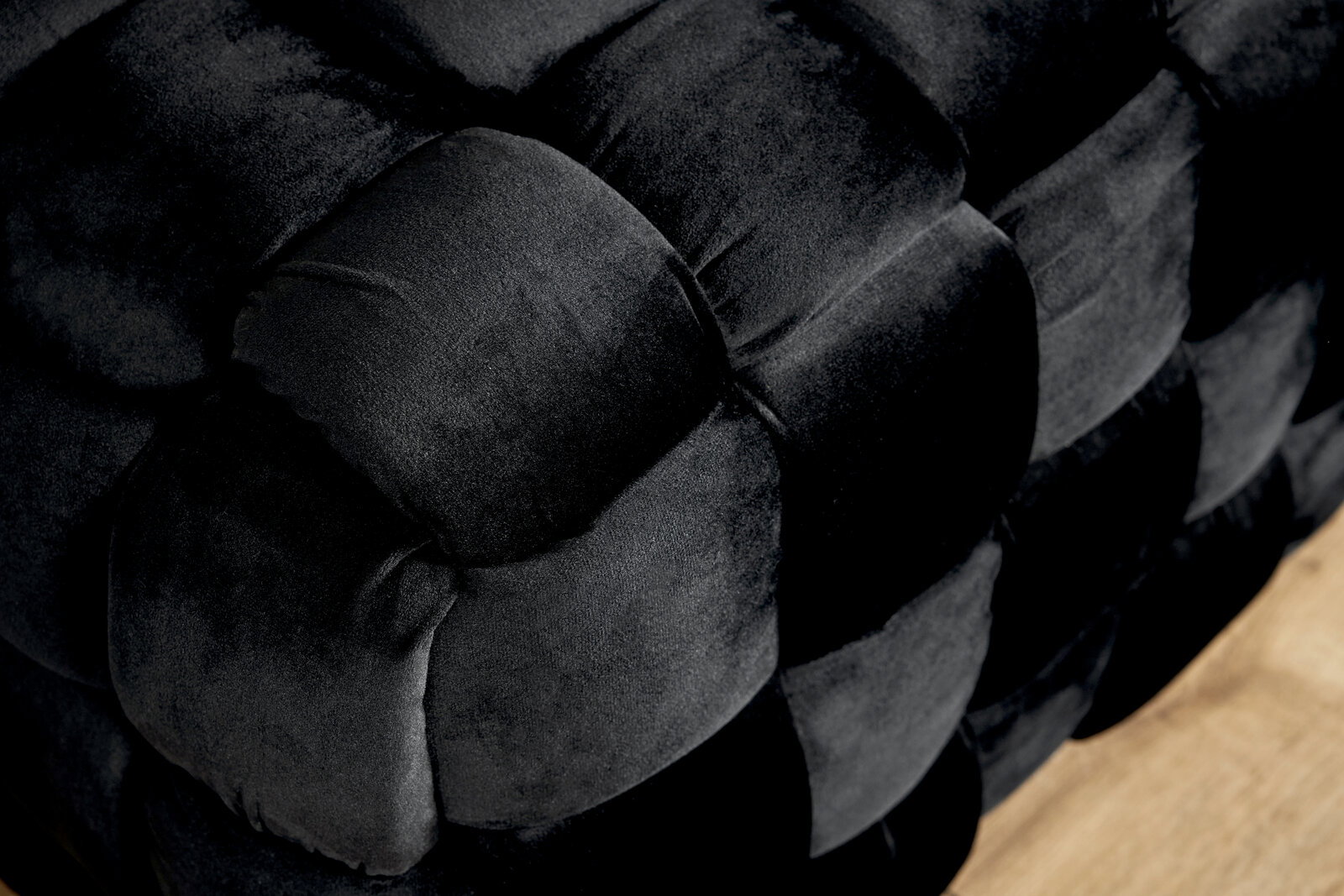 Nahaufnahme eines schwarzen, gepolsterten Hockers mit geflochtenem Design, seitliche Perspektive.