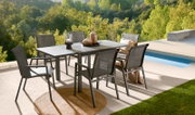 Een moderne tuintafel met zes stoelen op een terras met uitzicht op een groen bos en een zwembad, gefotografeerd vanuit een zijaanzicht.