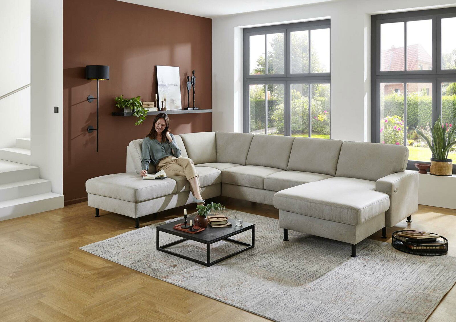 Moderne Polsterrundecke in einem hellen Wohnzimmer, seitliche Perspektive, mit einer Frau, die auf dem Sofa sitzt und ein Buch liest.