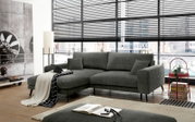 Graues Stoff-Ecksofa mit linksseitiger Ottomane und schwarzen Metallfüßen im modernen Wohnzimmer vor großen Fenstern, Ansicht schräg von vorne