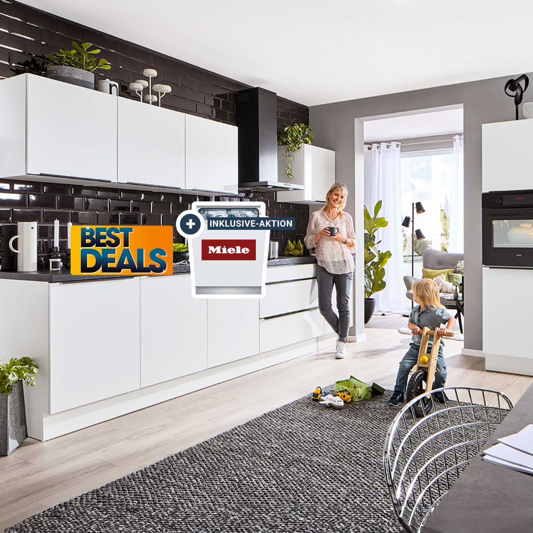 Moderne Küche mit weißen Schränken und dunkler Rückwand, Frau steht an der Arbeitsfläche, Kind spielt auf dem Boden