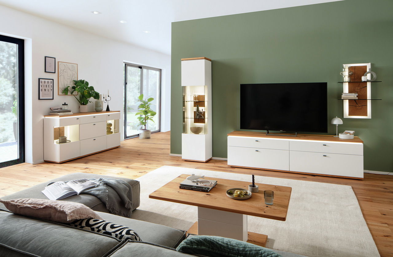 Modernes Wohnzimmer mit Sideboard in heller Holzoptik, frontal betrachtet. Das Sideboard steht links im Raum, dekoriert mit Pflanzen und Büchern.