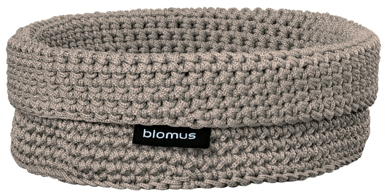 Grijze, gehaakte opbergmand met omgeslagen rand en „blomus“-label, in vooraanzicht licht van bovenaf gefotografeerd op een witte achtergrond.