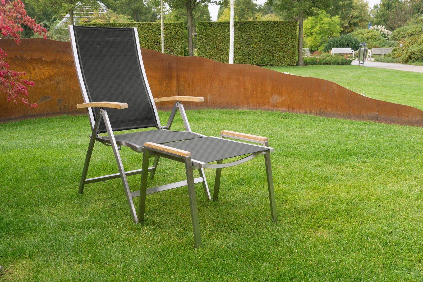 Moderner Hocker mit Metallrahmen und Holzarmlehnen, aufgestellt auf einer grünen Wiese, seitliche Perspektive
