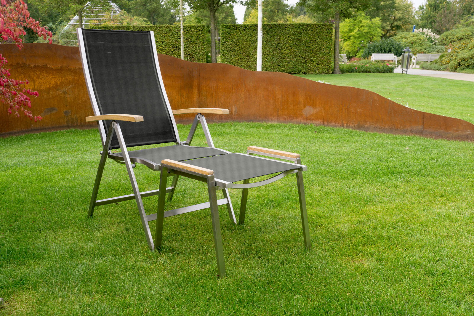 Zebra Hocker ONE Moderner Hocker mit Metallrahmen und Holzarmlehnen, aufgestellt auf einer grünen Wiese, seitliche Perspektive