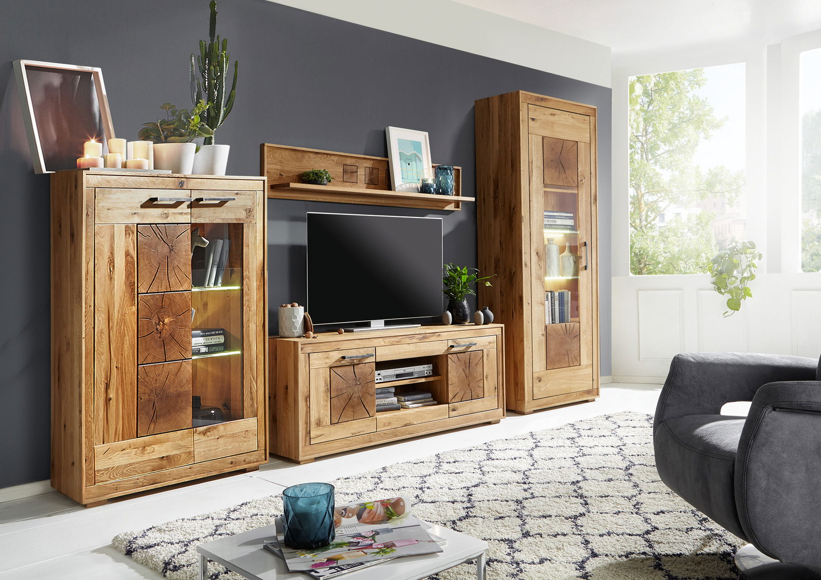 Wohnzimmeransicht mit moderner Holzmöbelkombination, bestehend aus Vitrine, TV-Element und Wandboard, in natürlichem Holzton. Perspektive von vorne.