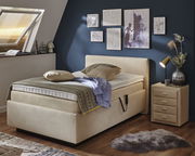 Gemütliches Polsterbett in einem stilvoll eingerichteten Schlafzimmer mit blauer Wand, dekorativen Bildern und einem Nachttisch. Perspektive von der Seite.