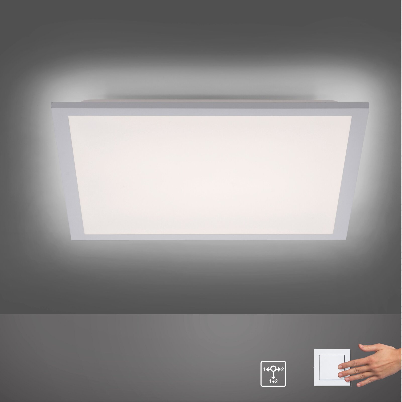 Rechteckige LED-Deckenleuchte/Panel mit weißem Rahmen und diffuser Lichtfläche, eingeschaltet, in frontaler Ansicht von unten an der Decke; unten rechts ein Wandschalter mit Hand.