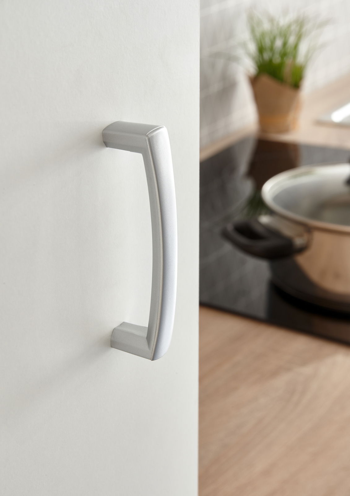 Nahaufnahme eines silbernen Türgriffs an einem Küchenschrank, seitliche Perspektive mit einem Topf im Hintergrund.