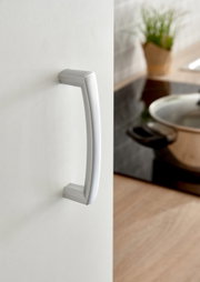 Nahaufnahme eines silbernen Türgriffs an einem Küchenschrank, seitliche Perspektive mit einem Topf im Hintergrund.