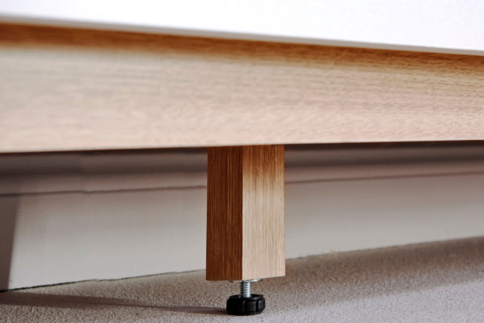 Nahaufnahme eines Holzfußes eines Sideboards mit verstellbarem Kunststofffuß auf Teppichboden.
