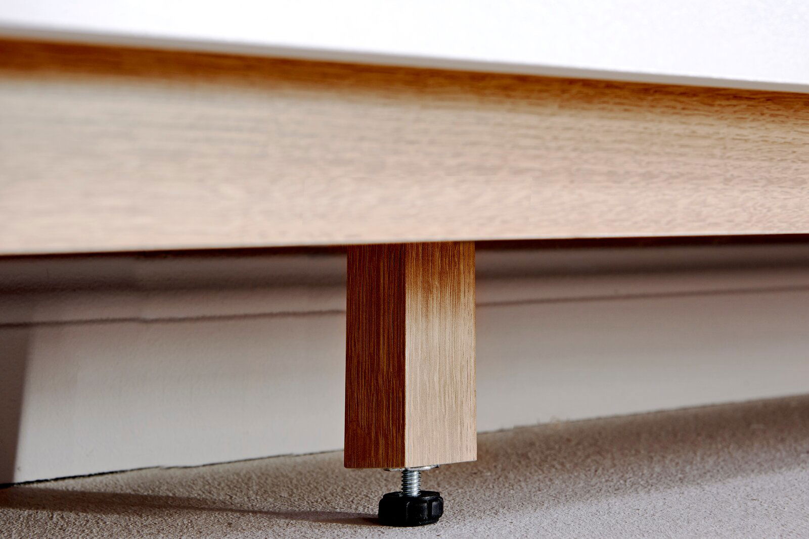 Nahaufnahme eines Holzfußes eines Sideboards mit verstellbarem Kunststofffuß auf Teppichboden.