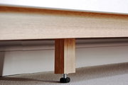 Nahaufnahme eines Holzfußes eines Sideboards mit verstellbarem Kunststofffuß auf Teppichboden.