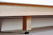 Nahaufnahme eines Holzfußes eines Sideboards mit verstellbarem Kunststofffuß auf Teppichboden.