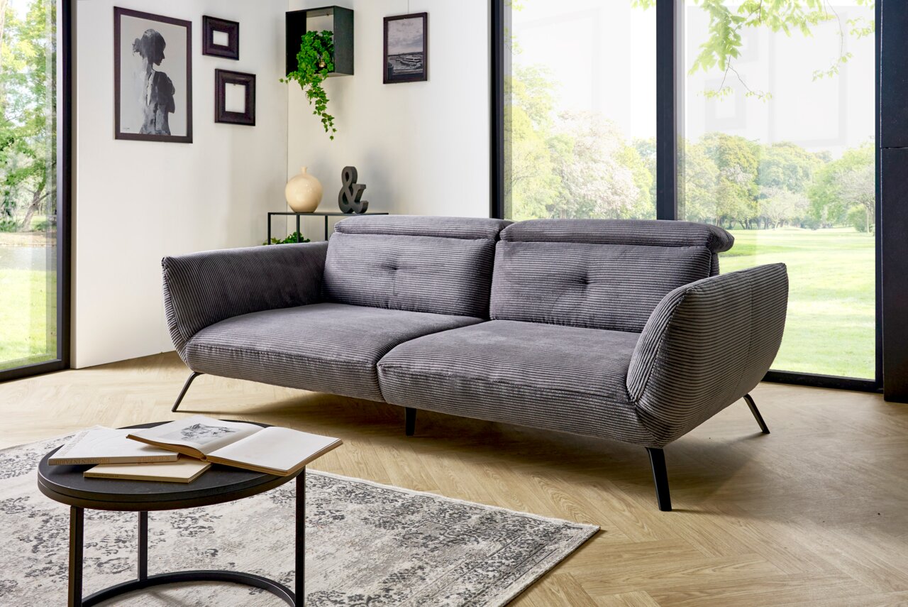 Graues Megasofa in einem modernen Wohnzimmer mit großen Fenstern, seitliche Perspektive