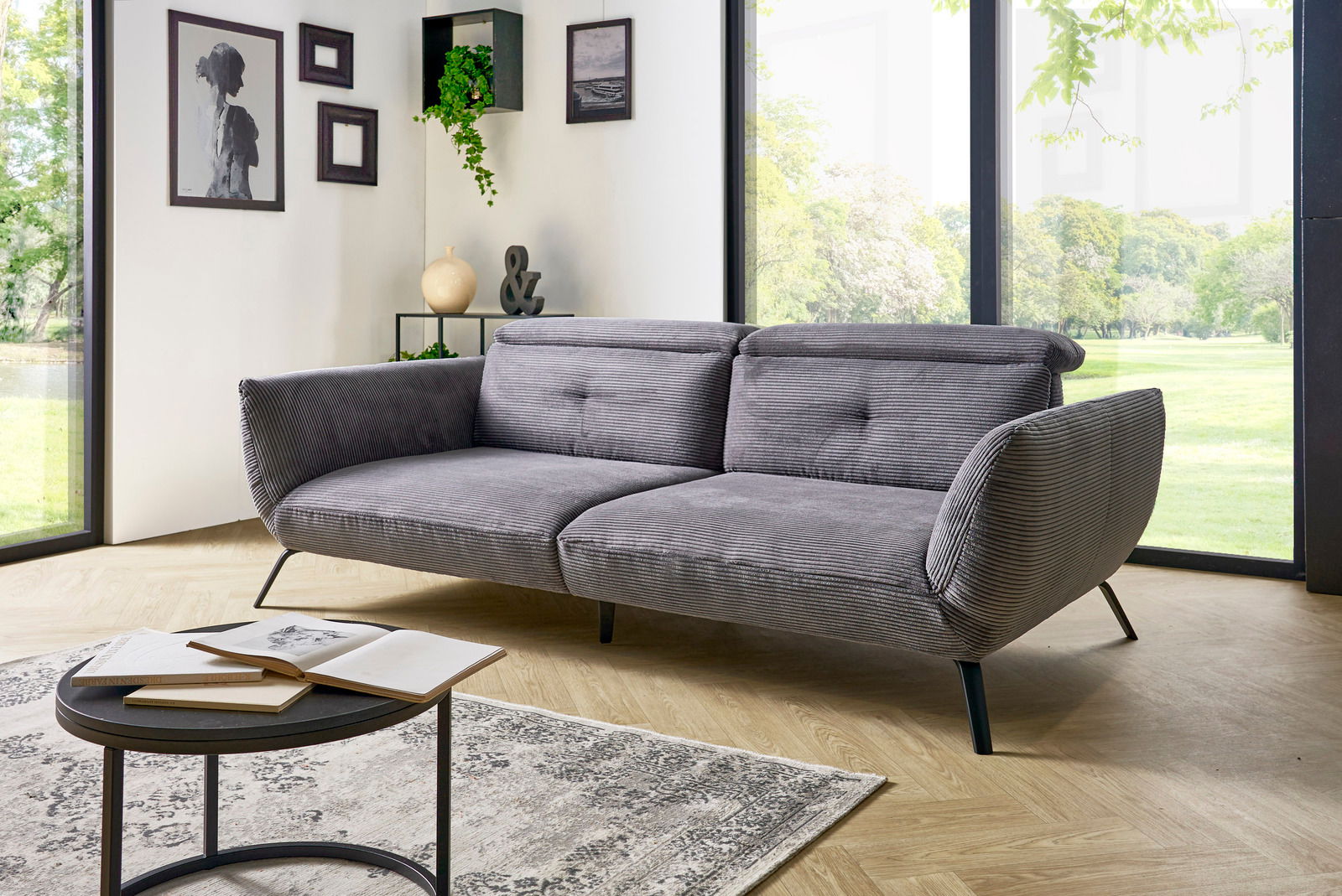 Graues Megasofa in einem modernen Wohnzimmer mit großen Fenstern, seitliche Perspektive