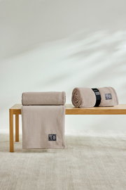 Zwei beige s.Oliver Kuscheldecken auf einer Holzbank, eine gefaltet und eine gerollt, in einem hellen Raum.