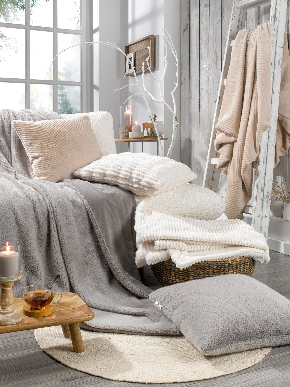 Linneweber Felldecke ca.150x200cm Gemütliche Wohnzimmerszene mit verschiedenen Fellkissen und Decken in neutralen Tönen, arrangiert auf einem Sofa und einem Korb, mit Kerzen und Dekoration im Hintergrund. Perspektive von vorne.