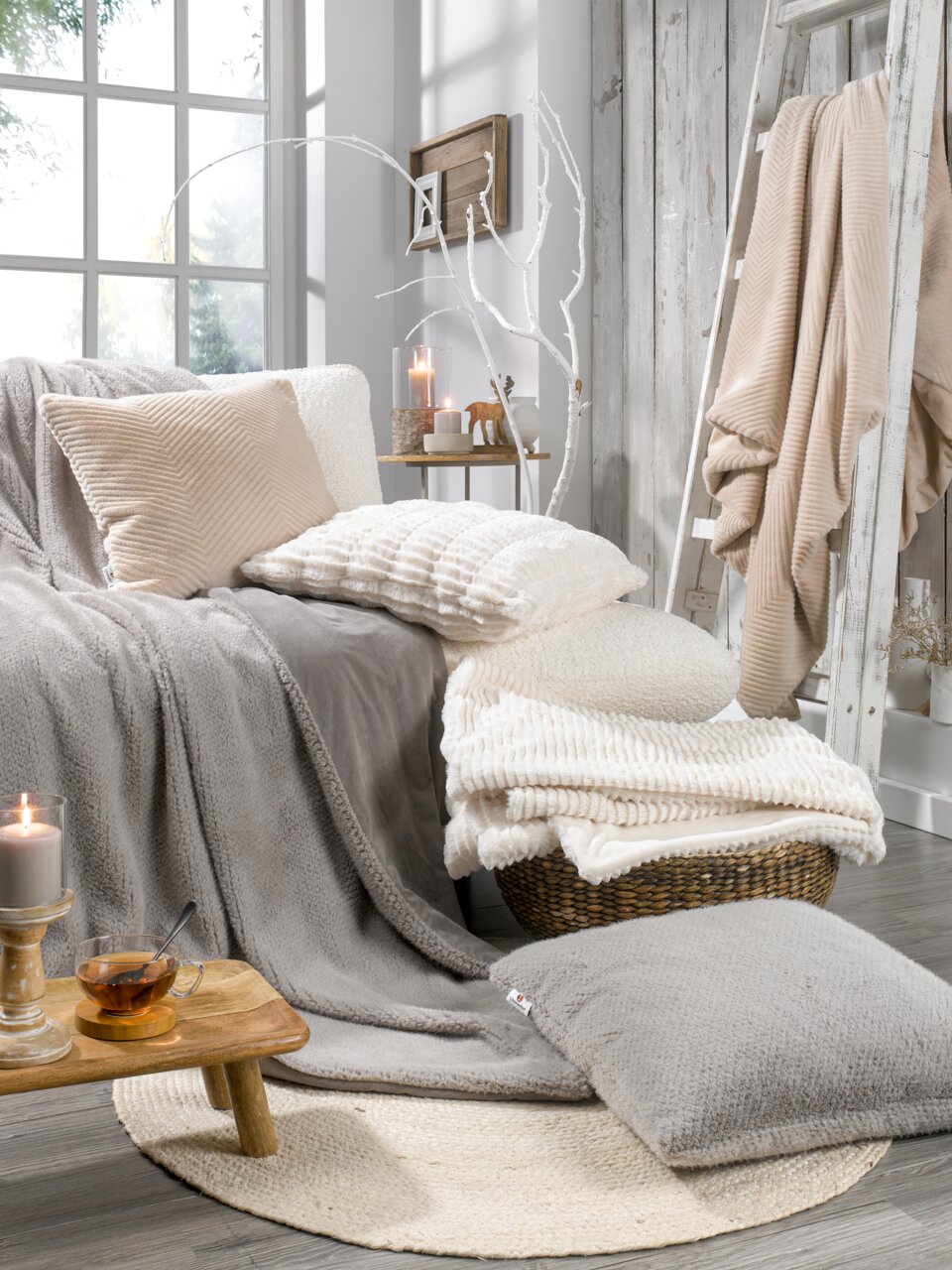 Linneweber Felldecke ca.150x200cm Gemütliche Wohnzimmerszene mit verschiedenen Fellkissen und Decken in neutralen Tönen, arrangiert auf einem Sofa und einem Korb, mit Kerzen und Dekoration im Hintergrund. Perspektive von vorne.