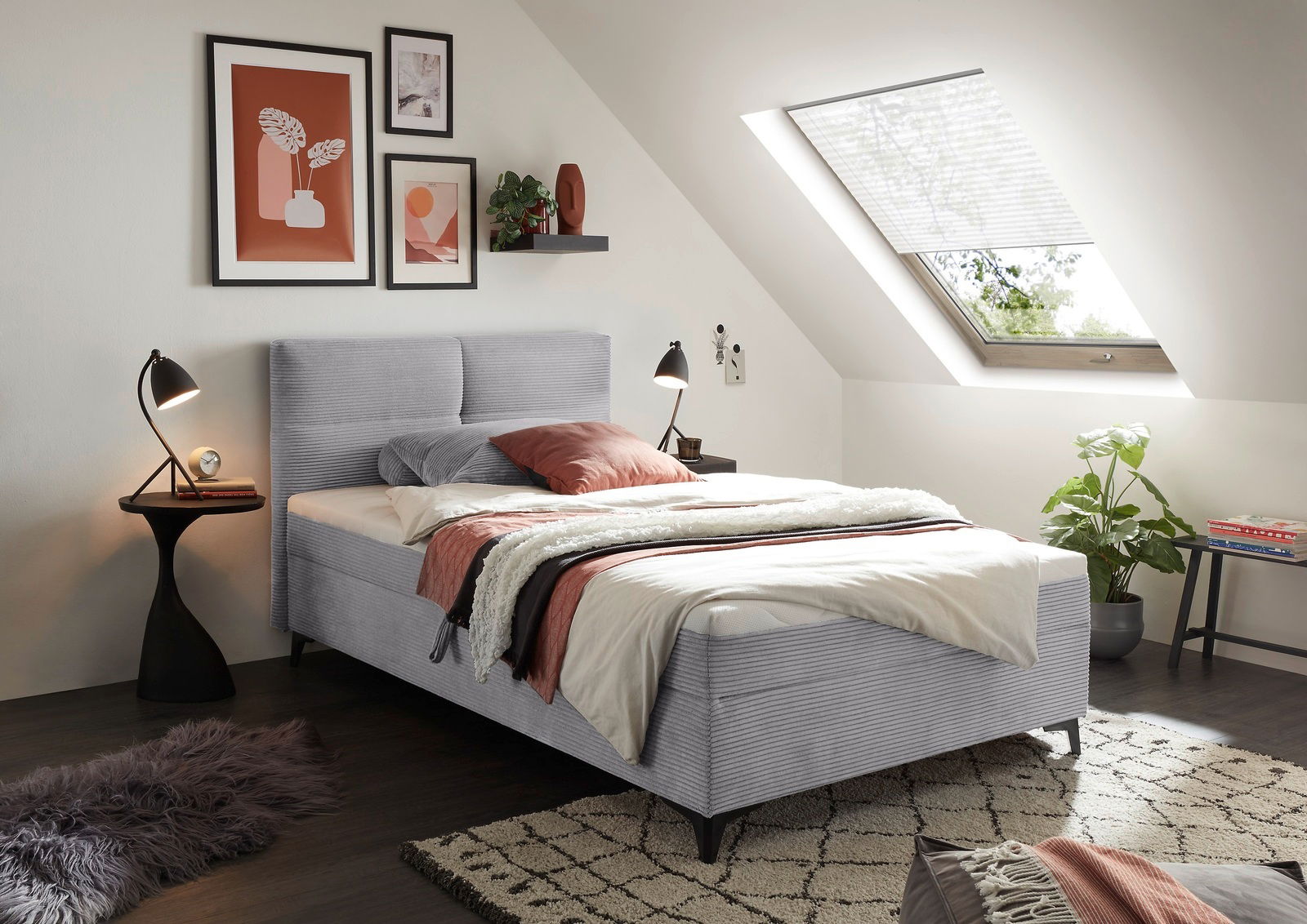 Gemütliches Boxbett in einem modernen Schlafzimmer mit schrägem Dachfenster, dekoriert mit stilvollen Bildern und Pflanzen, seitliche Perspektive.