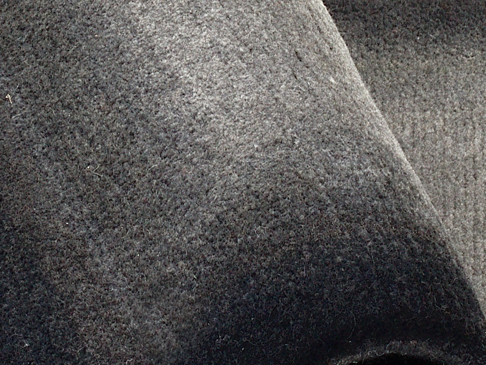 Nahaufnahme eines grauen Wollteppichs mit weicher Textur, von oben betrachtet.