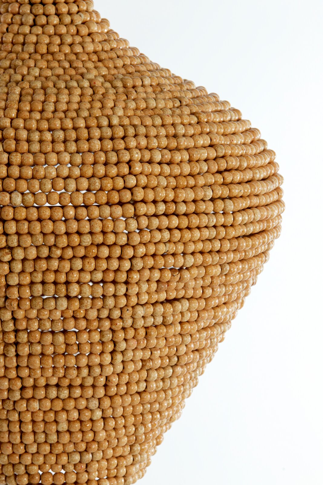 Close-up van een hanglamp met een oppervlak van kleine, ronde houten kraaltjes, die een warme, natuurlijke textuur creëren.