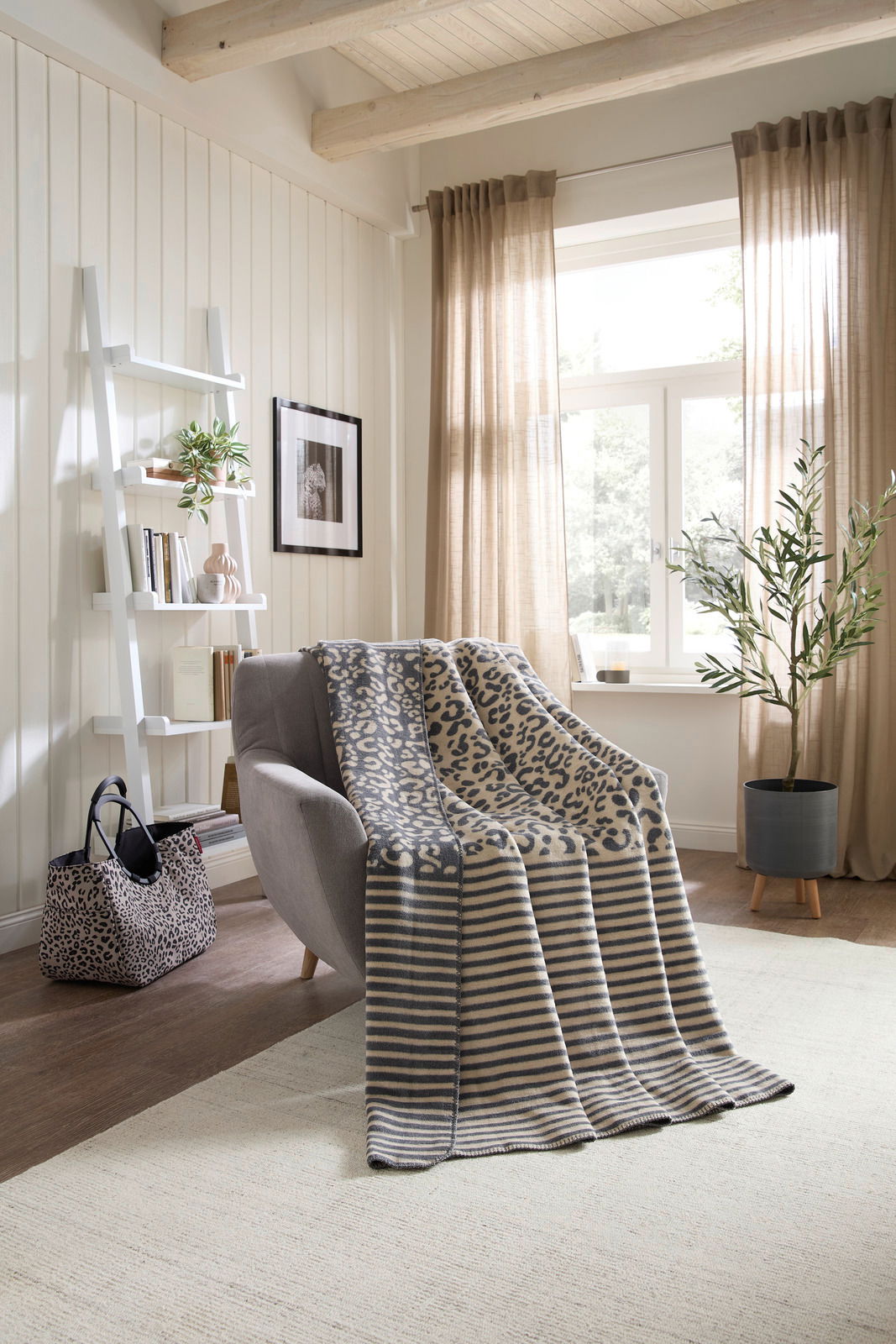 Linneweber Wohndecke LEO Gemütliche Wohndecke mit Leopardenmuster und Streifen auf einem Sessel in einem hellen Wohnzimmer, seitliche Perspektive.
