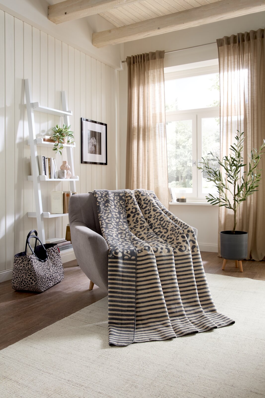 Gezellige woondeken met luipaardprint en strepen op een fauteuil in een lichte woonkamer, gezien vanuit de zijkant.