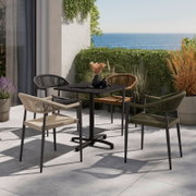Vier stilvolle Stapelsessel in verschiedenen Farben um einen modernen Tisch auf einer Terrasse mit Meerblick, aus seitlicher Perspektive.