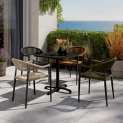 Vier stijlvolle stapelstoelen in verschillende kleuren rond een moderne tafel op een terras met uitzicht op zee, gezien vanuit de zijkant.