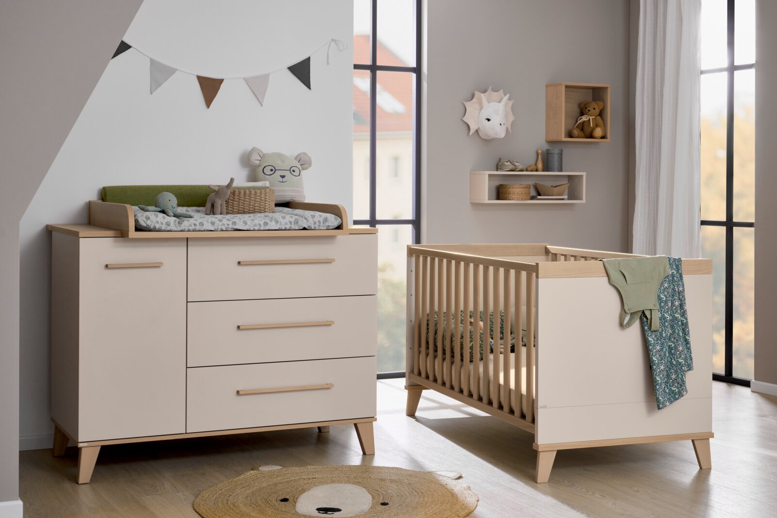Kinderkamer met commode en ledikantje van lichtgekleurd hout, vierkante wandkast aan de muur, aanzicht van voren
