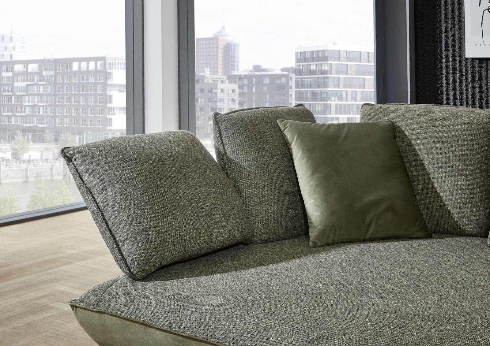 Grüne Longchairkombination mit weichen Kissen, seitliche Perspektive, im modernen Wohnzimmer mit großen Fenstern.