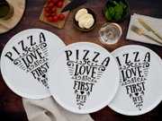 Drei weiße Pizzateller mit schwarzem Schriftzug „PIZZA LOVE AT FIRST BITE“ auf rustikalem Holztisch, Draufsicht von oben.