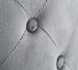 Nahaufnahme eines grauen, gepolsterten Hockers mit Knopfdetails und Kreuzstichnähten.