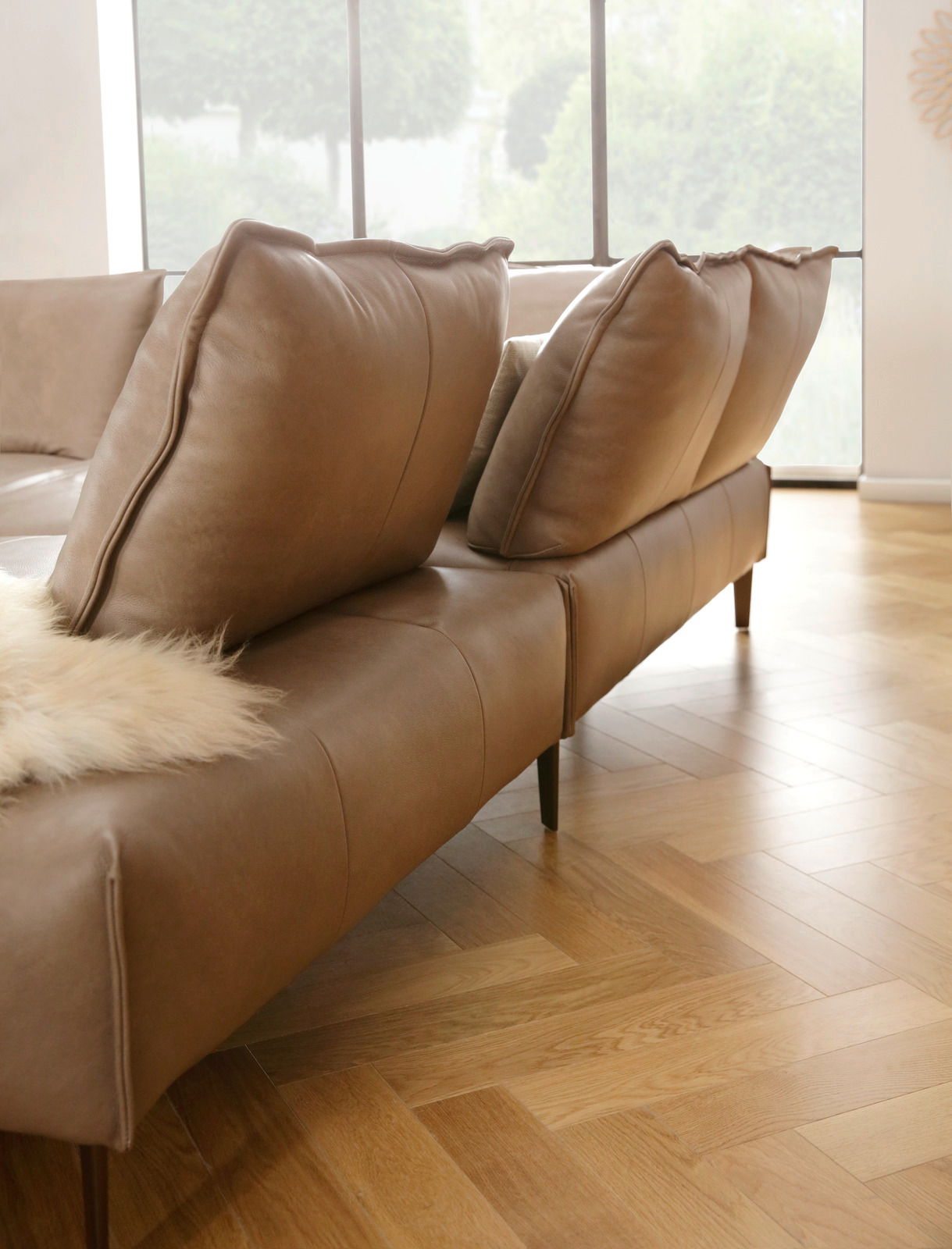 Braune Polsterrundecke mit großen Kissen, seitliche Perspektive, auf Parkettboden in einem hellen Raum.