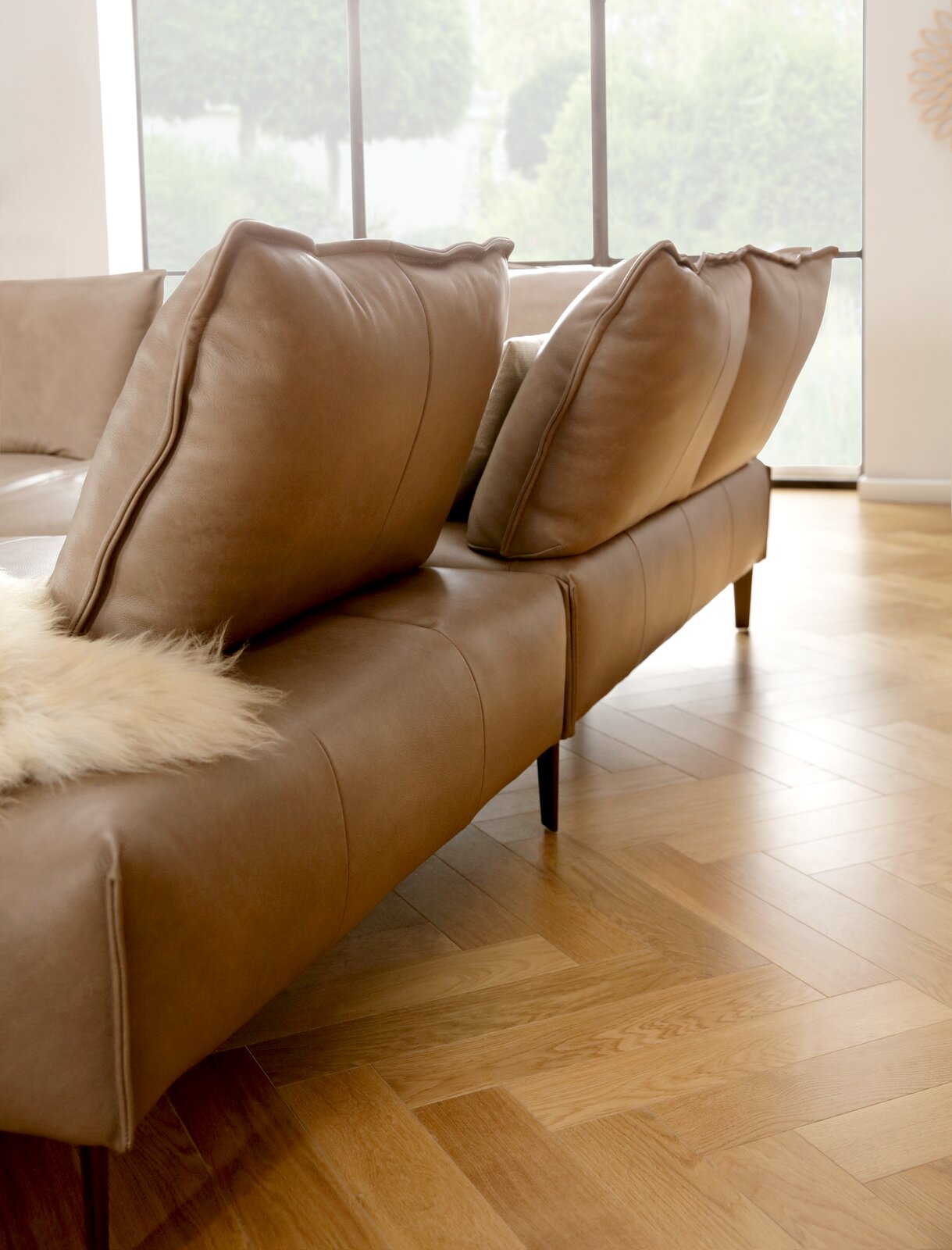 Braune Polsterrundecke mit großen Kissen, seitliche Perspektive, auf Parkettboden in einem hellen Raum.