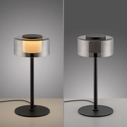 Moderne Tischleuchte RIKA mit zylindrischem Glaslampenschirm und schwarzem Metallfuß, seitliche Perspektive.