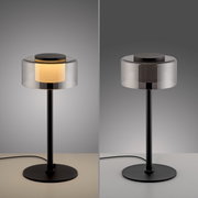 Moderne Tischleuchte RIKA mit zylindrischem Glaslampenschirm und schwarzem Metallfuß, seitliche Perspektive.