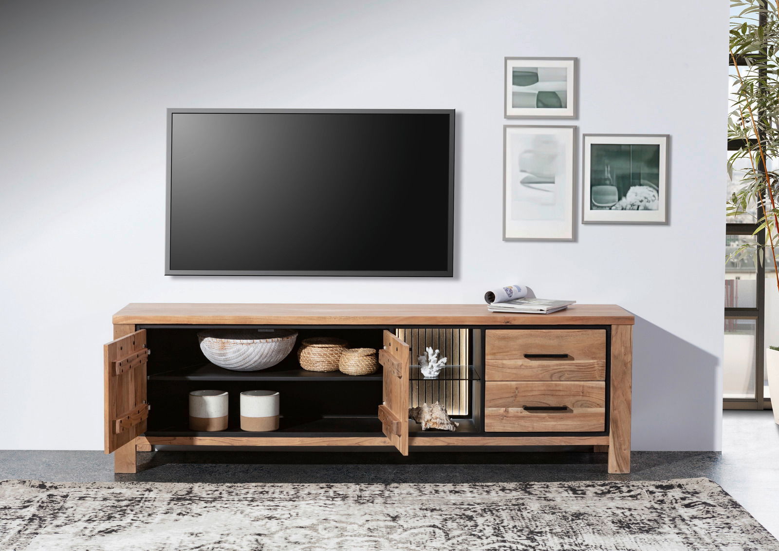 Frontale Ansicht eines Lowboards aus Holz mit offenen Türen, dekoriert mit Körben und Keramik, unter einem an der Wand montierten Fernseher.