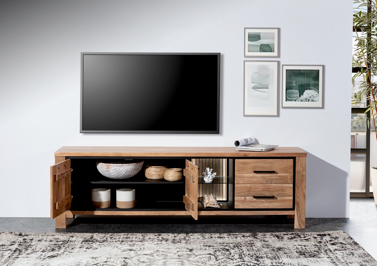 Frontale Ansicht eines Lowboards aus Holz mit offenen Türen, dekoriert mit Körben und Keramik, unter einem an der Wand montierten Fernseher.