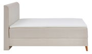 Seitliche Ansicht eines Boxspringbetts mit hellem Stoffbezug und Holzfüßen.